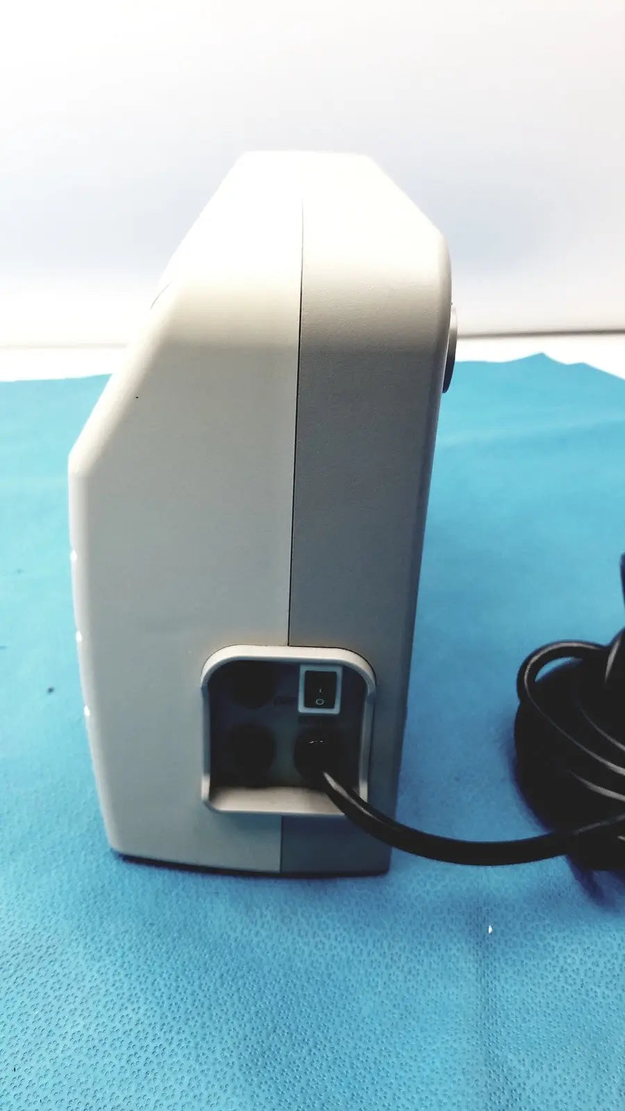 White and gray medical equipment air pump sizewise medical equipment with black power cord plugged into rear port