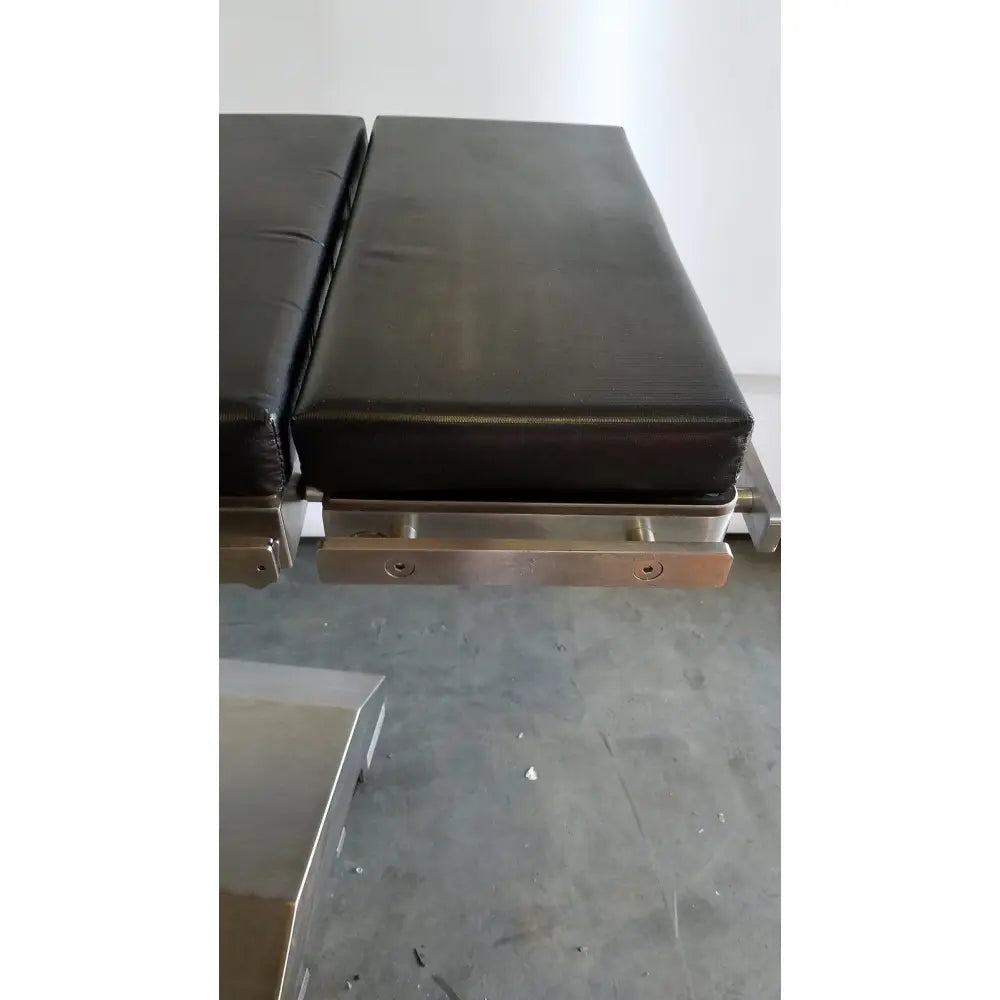 Black padded skytron 1700 surgical table with stainless steel frame and hand control for medical equipment use