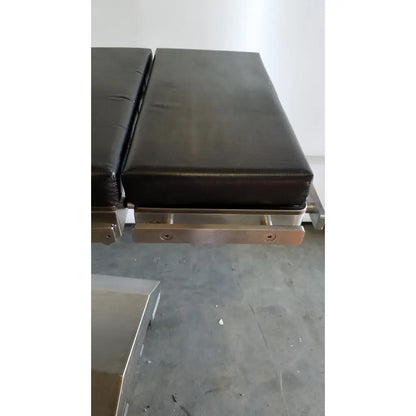 Black padded skytron 1700 surgical table with stainless steel frame and hand control for medical equipment use