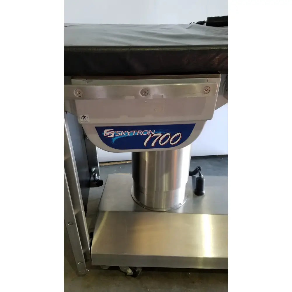 Silver metallic skytron 1700 surgical table with hand control and blue and white label medical equipment
