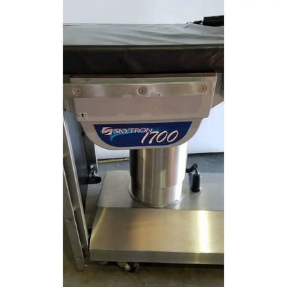 Silver metallic skytron 1700 surgical table with hand control and blue and white label medical equipment