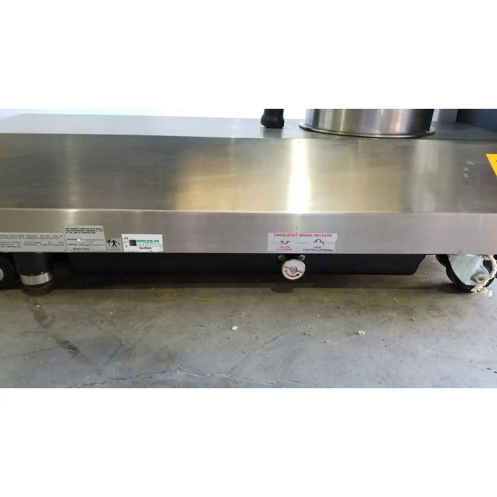 Stainless steel surgical table with polished countertop and black undercarriage featuring hand control for reuse medical use