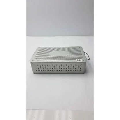 Solid brass sterilization storage container with lid featuring a silver metallic perforated surgical instrument tray and handle