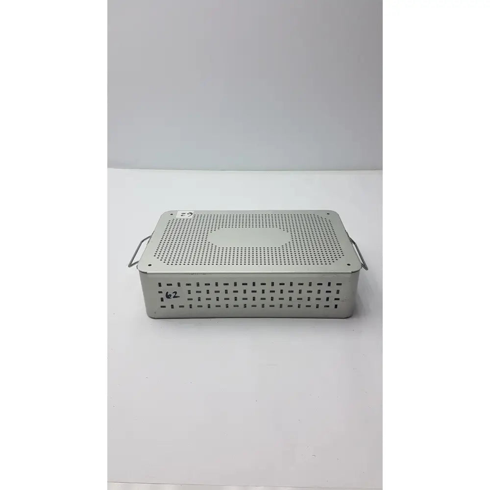 Solid brass sterilization storage container with lid and perforated silver metallic surgical instrument tray with side handles