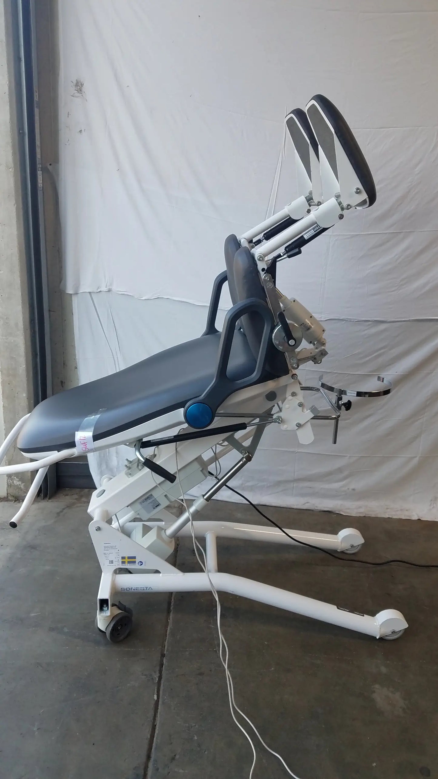 White medical examination table with black padded surface and adjustable armrests in sonesta s3 ultimate patient positioning procedure chair