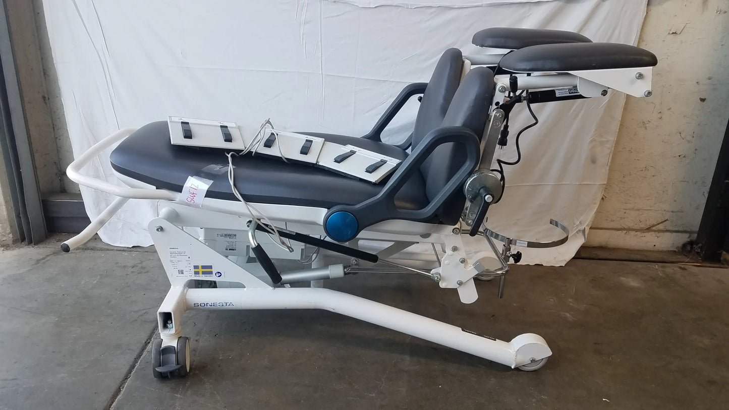 White medical procedure chair with black padded surfaces and adjustable components for ultimate patient positioning