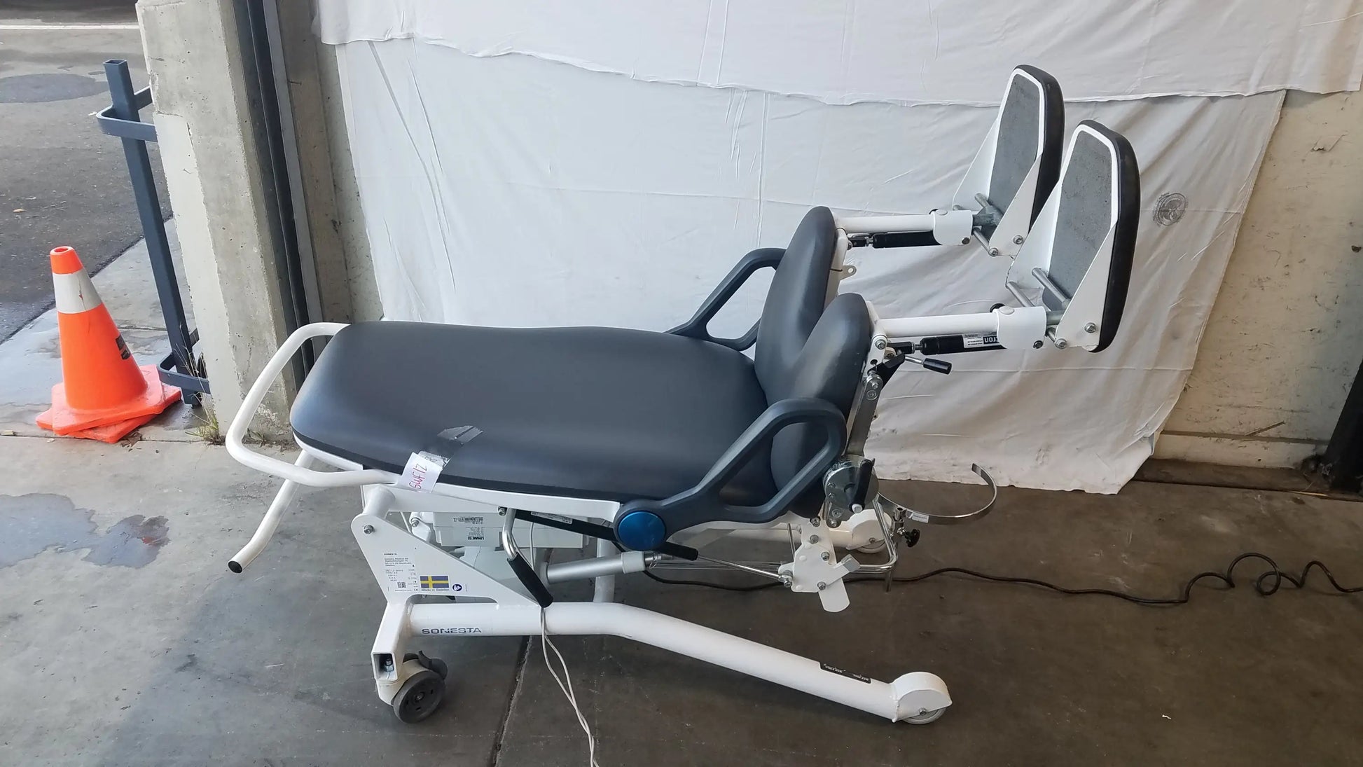 Sonesta S3 ultimate patient positioning procedure chair with white frame, black padded seat, adjustable armrests, and wheels