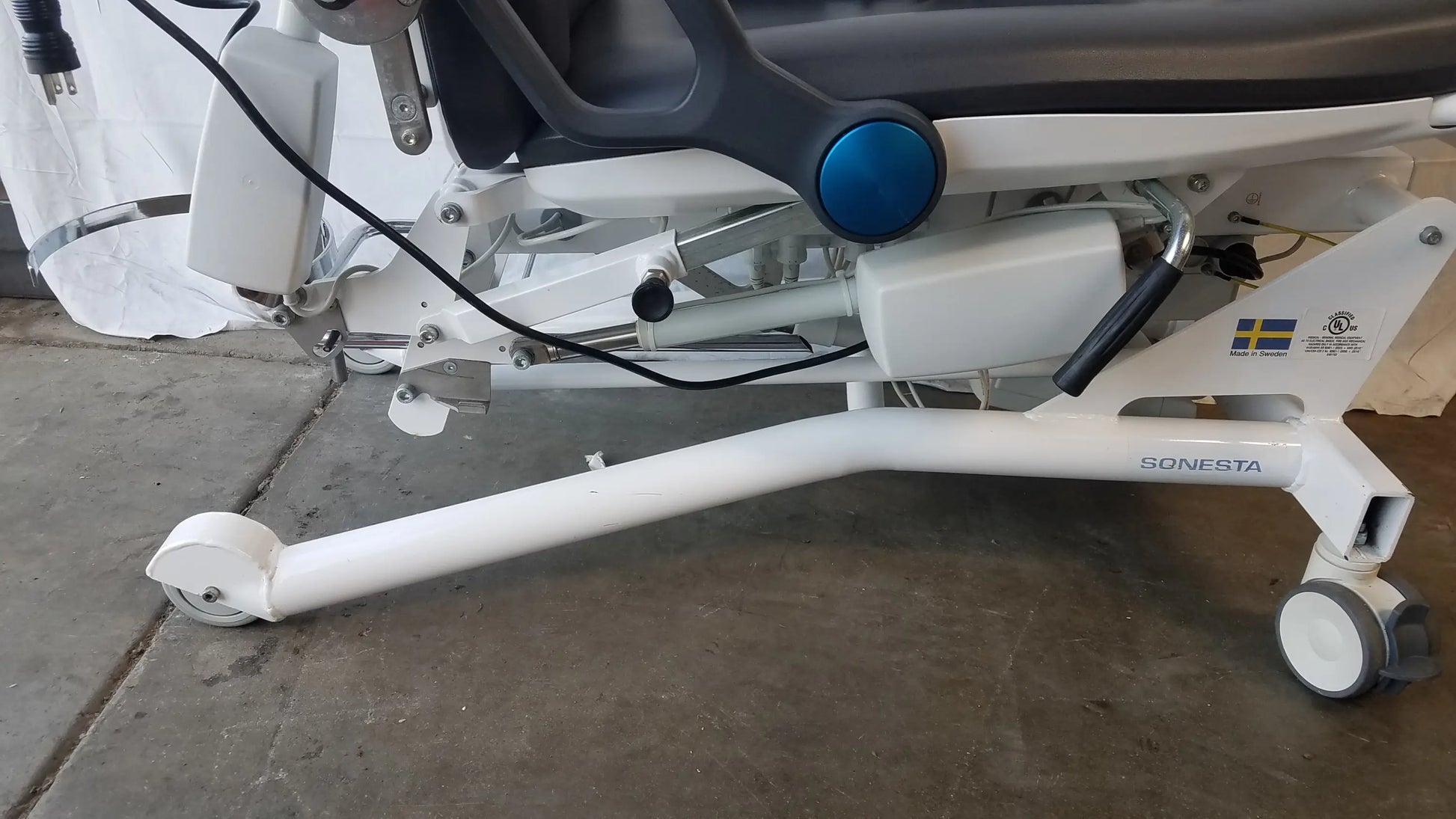 White Sonesta S3 ultimate patient positioning procedure chair with blue circular control knob and wheeled base for patient positioning