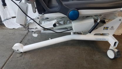White Sonesta S3 ultimate patient positioning procedure chair with blue circular control knob and wheeled base for patient positioning