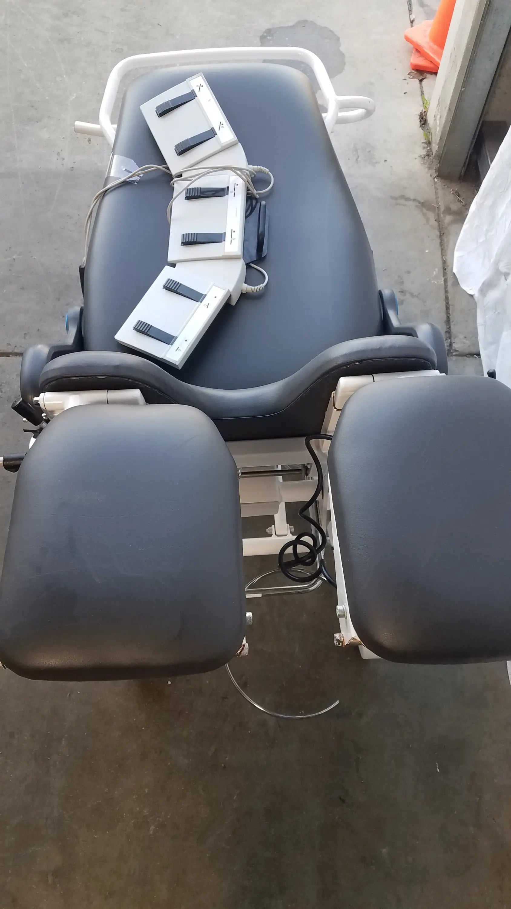 Black padded Sonesta S3 ultimate patient positioning procedure chair with white metal frame and adjustable footrests