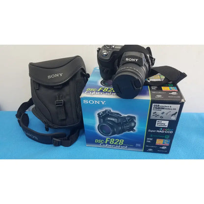 Black sony cyber-shot dsc-f828 digital camera with lens cap on resting on original blue packaging with ac adapter