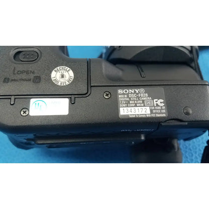 Black Sony Cyber-shot DSC-F828 digital still camera with matte finish and visible model label featuring AC power adapter