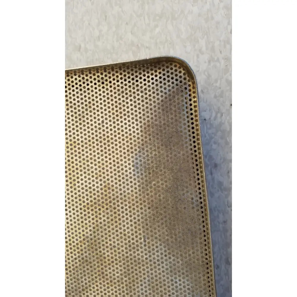 A golden perforated rectangular stainless steel sterilization basket tray with slightly worn edges for steel sterilization