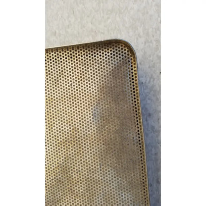 A golden perforated rectangular stainless steel sterilization basket tray with slightly worn edges for steel sterilization
