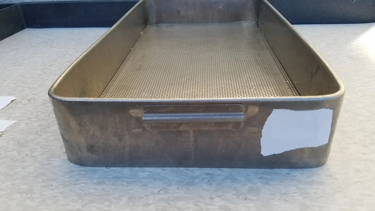 A rectangular stainless steel sterilization basket tray with perforated mesh and sturdy handle showing signs of wear