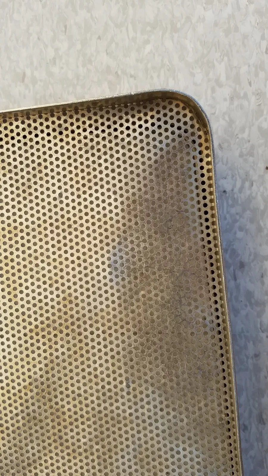 A golden perforated rectangular stainless steel sterilization basket tray with slightly worn edges for steel sterilization