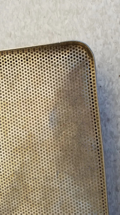 A golden perforated rectangular stainless steel sterilization basket tray with slightly worn edges for steel sterilization