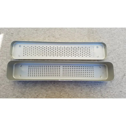Two rectangular silver steel healthcare equipment trays with perforated surfaces for medical sterilization use