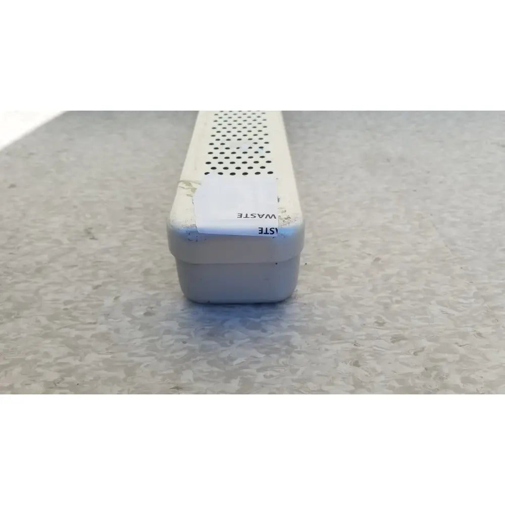 White plastic drainage grate with perforated top and chipped edges in steel healthcare equipment medical sterilization tray