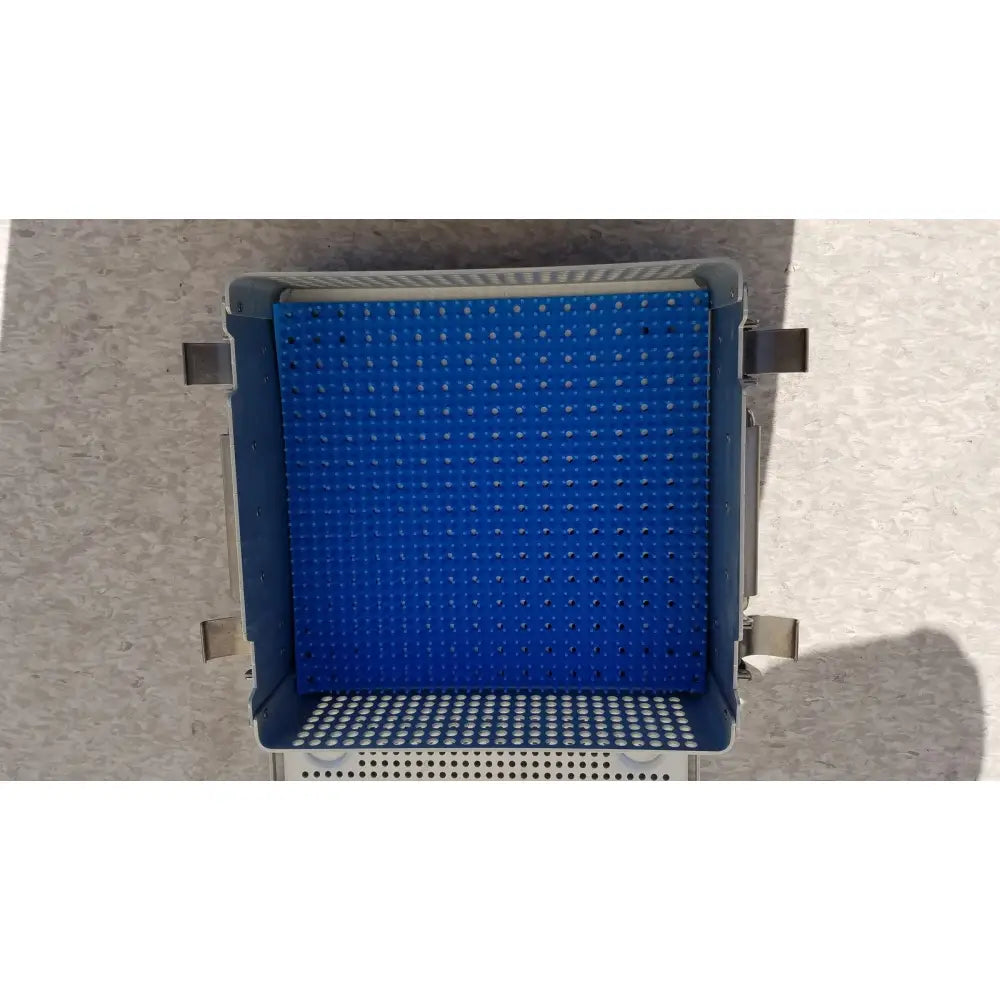 Blue plastic sterilization case with perforated top and bottom, dark gray metal frame, and reusable silicone mat