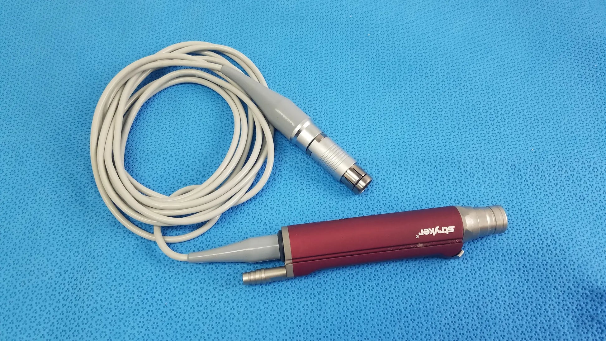 Red and gray Stryker 290-601-100 TPS Leibinger Hummer shaver handpiece with coiled white cable for surgical use