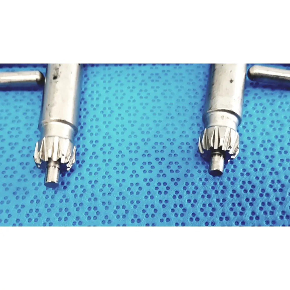 Two silver-toned metallic stryker chuck keys with machined teeth on a blue perforated surface for surgical drills