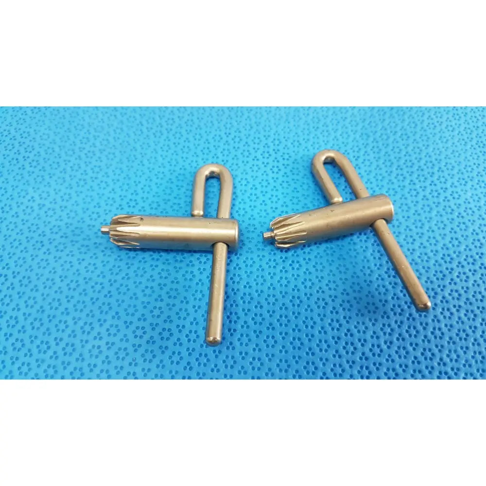 Two brushed gold metallic stryker chuck keys with star-shaped internal teeth for precision surgical drill use