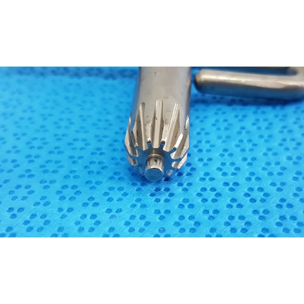 Metallic silver stryker chuck key with cylindrical shaft and teeth resting on a blue perforated surface for surgical drills
