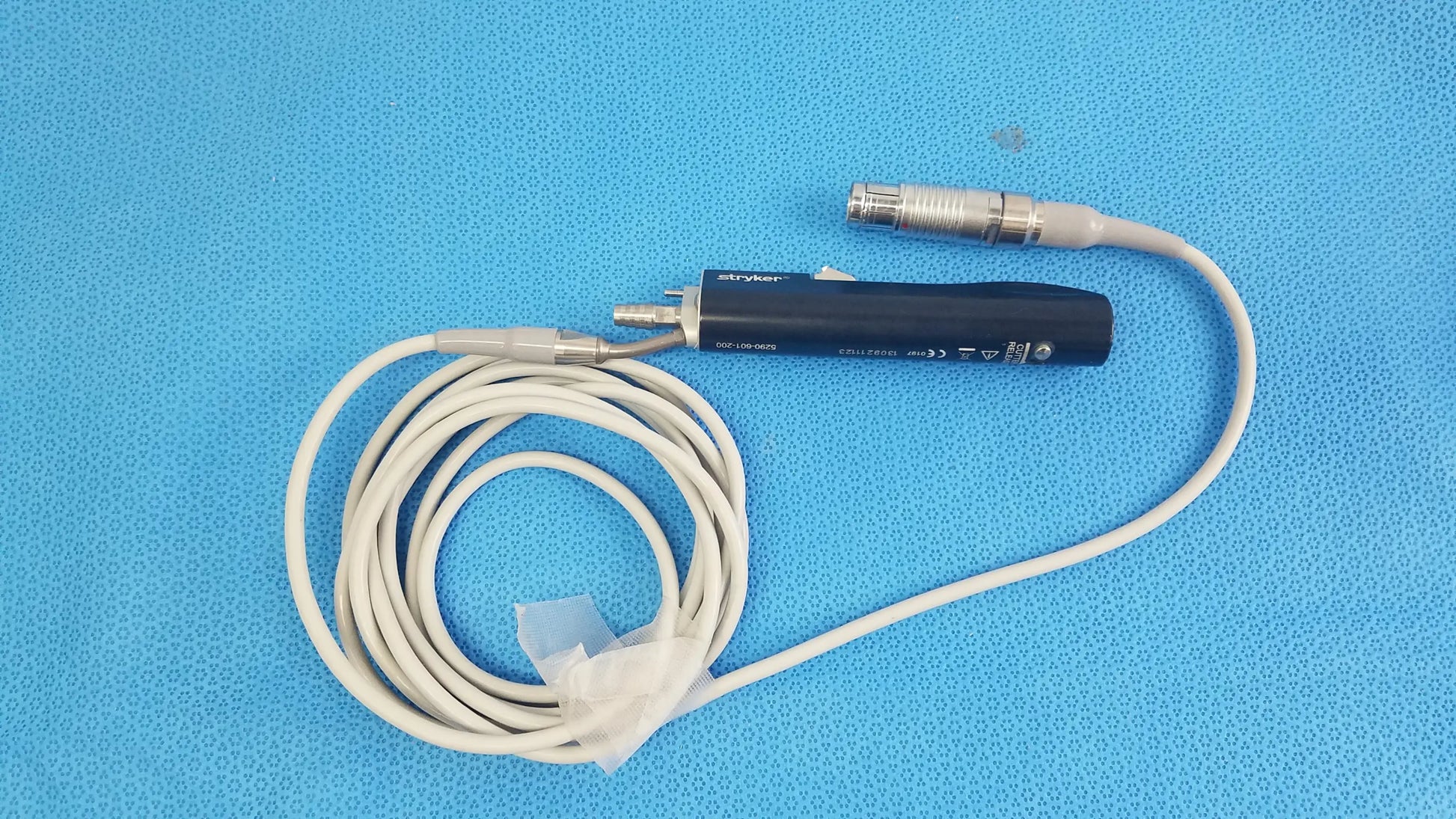 Black stryker essx microdebrider handpiece with coiled white cable and metallic connectors for reuse medical equipment