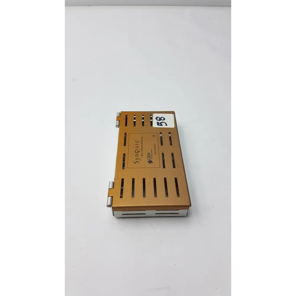 Gold-colored metal synovis gem precision surgical instrument case with hinged lid and ventilation slits for microtray organization