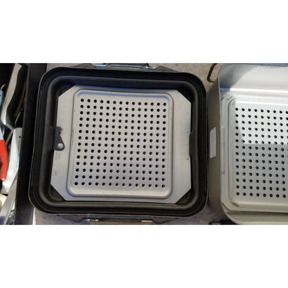 Silver perforated metal baking tray with black rubberized rim in the case genesis sterilization container with basket