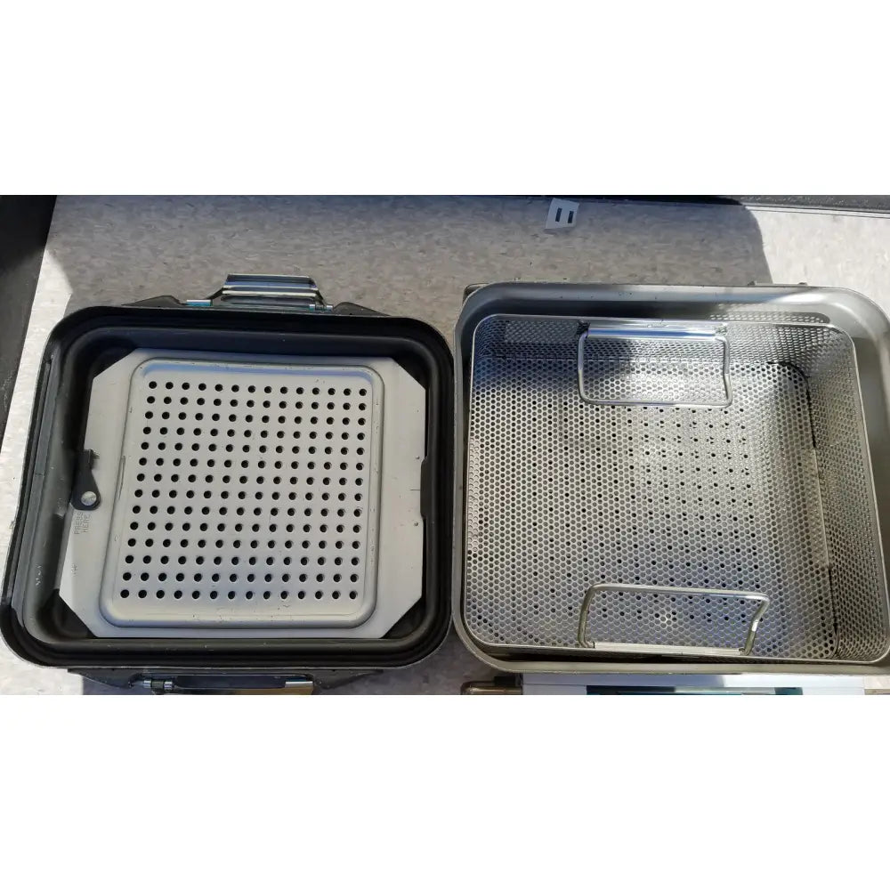 Silver perforated metal sterilization basket with reinforced handle and grid pattern in case genesis sterilization container