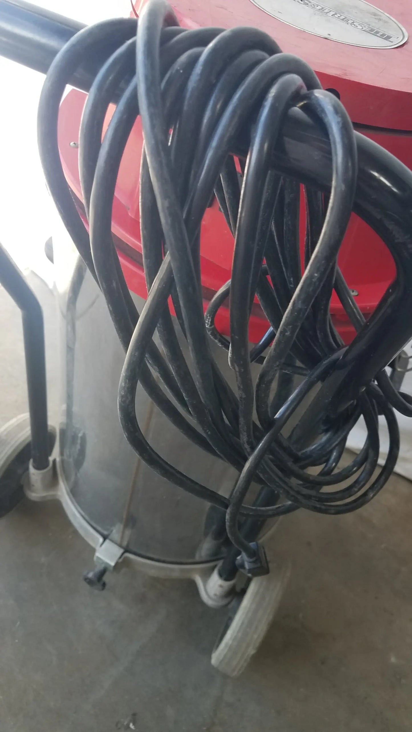 Coiled black rubber hose wrapped around red and gray surtec system 450m wet dry drum vacuum cleaner
