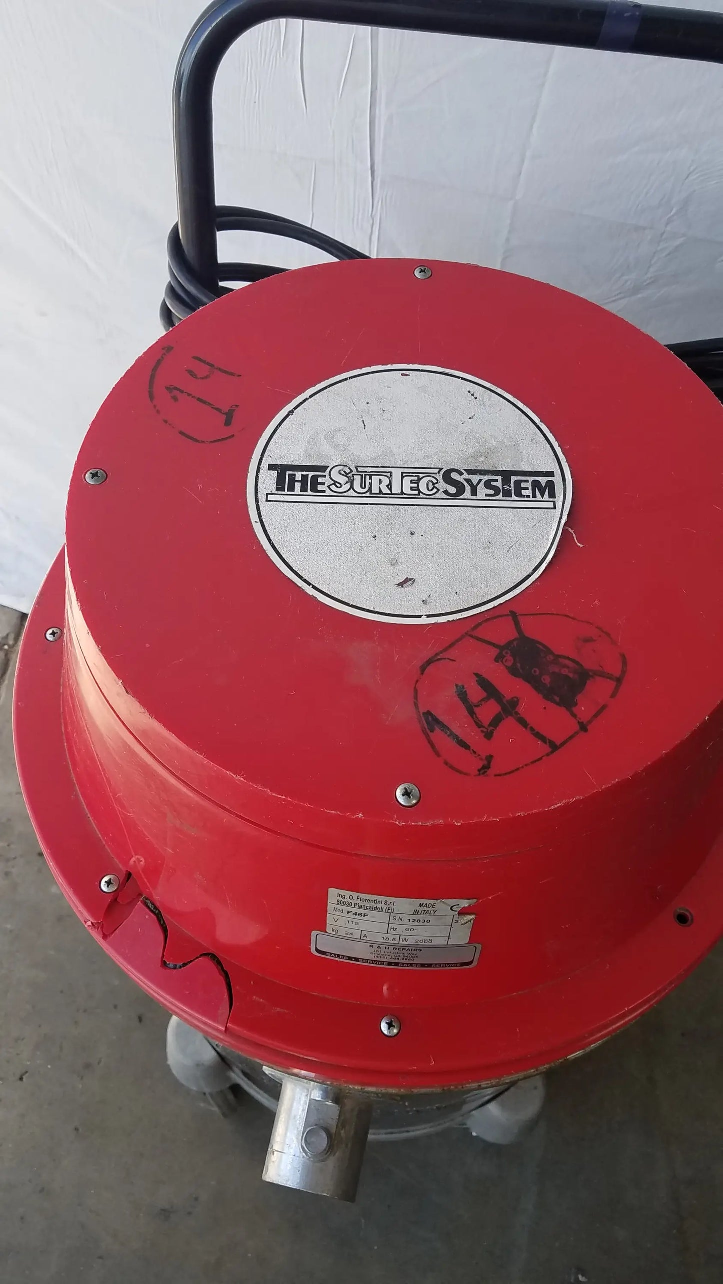 Red cylindrical wet dry drum vacuum cleaner with black handle and silver metal nozzle branded the sure system
