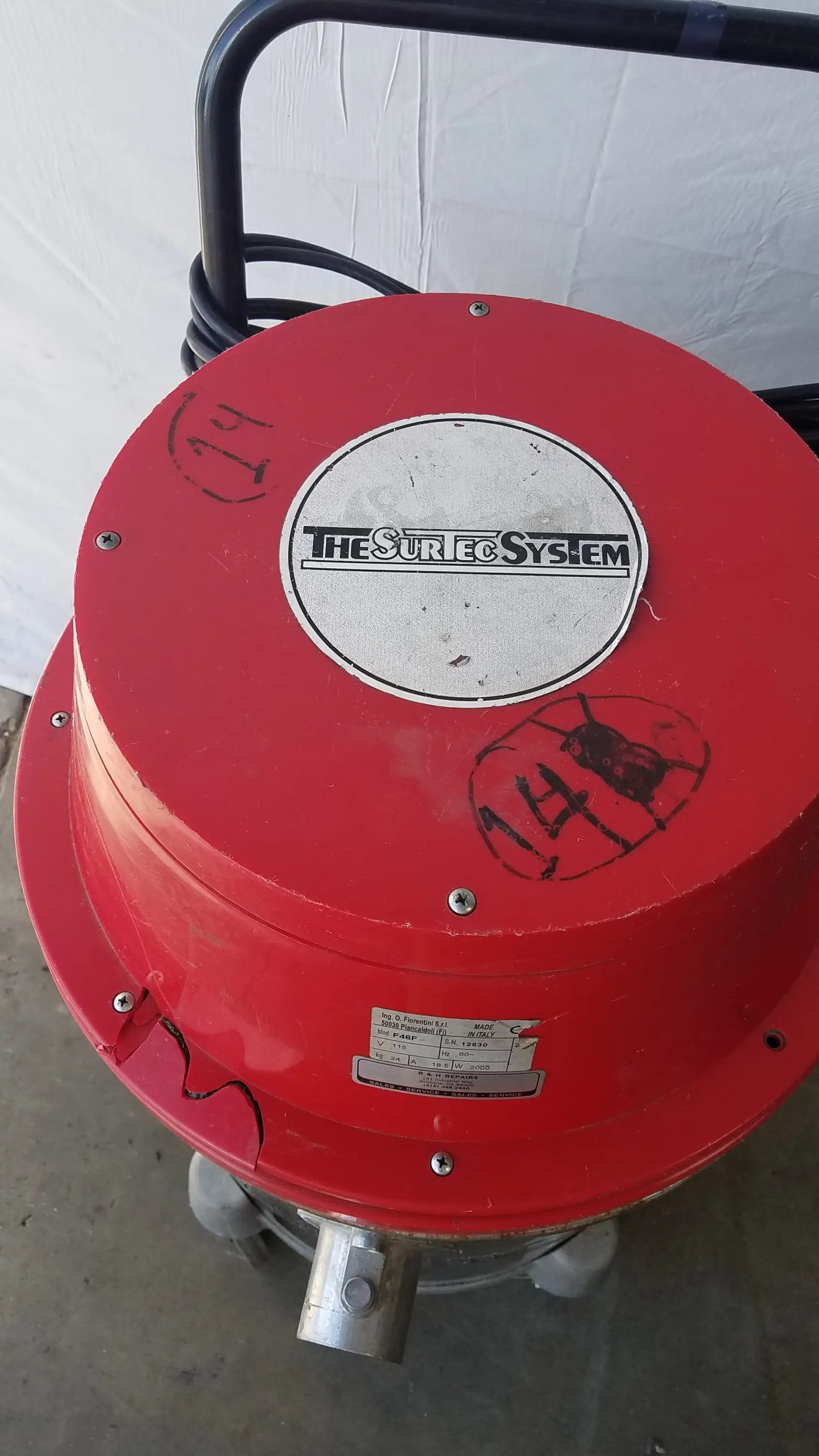 Red cylindrical wet dry drum vacuum cleaner with black handle and silver metal nozzle branded the sure system