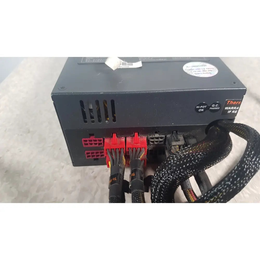 Rear view of black thermaltake 1350w toughpower gf3 power supply with red and black cables connected to ports