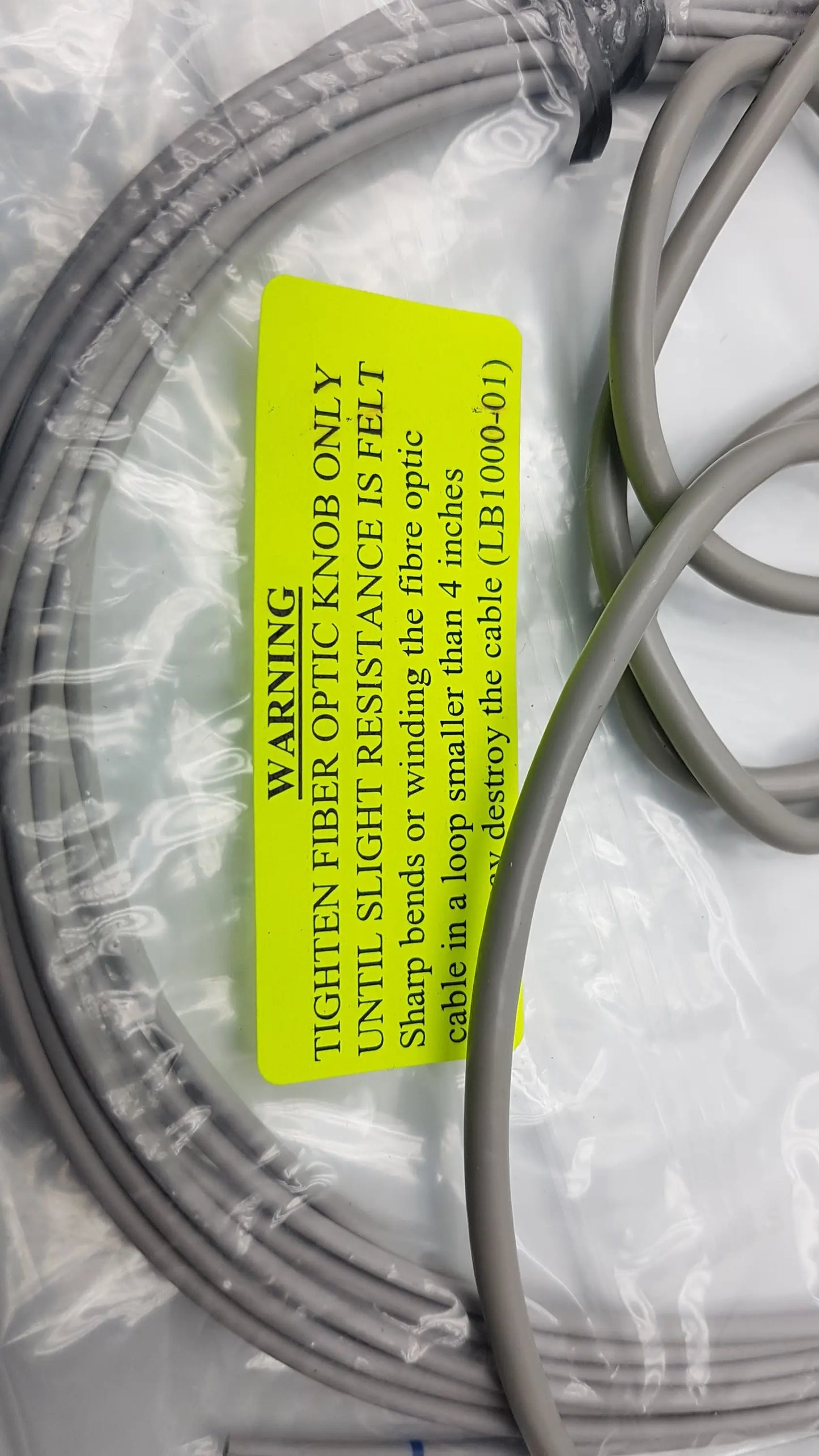Gray fiber optic cable with yellow warning label coiled in clear plastic for thought technology data acquisition system