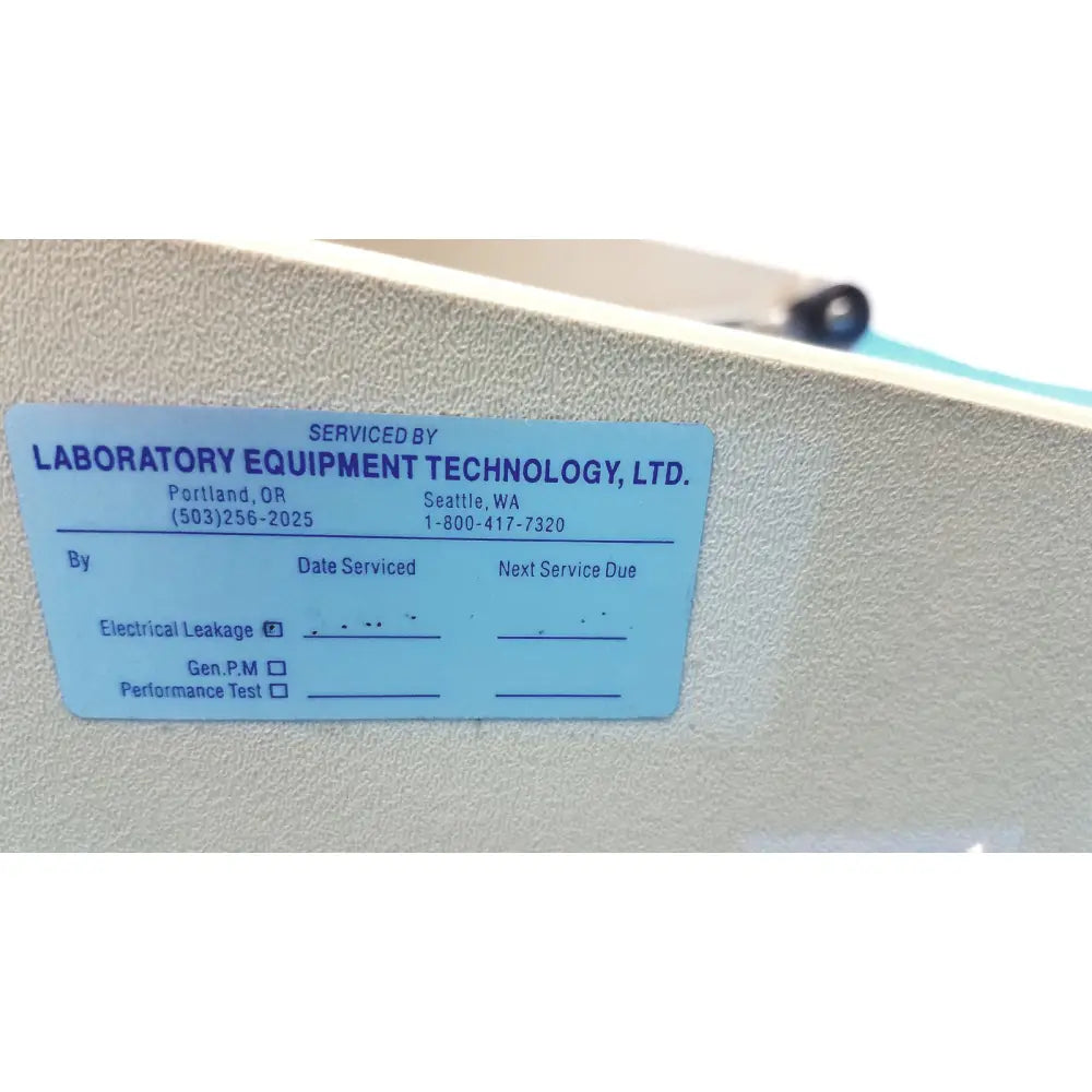Light blue rectangular service label on textured beige surface of titmus optical titmus ii vision tester with controller