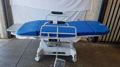 Blue padded TransMotion Medical TMM4 multi purpose stretcher chair with white metal frame and wheels for medical use