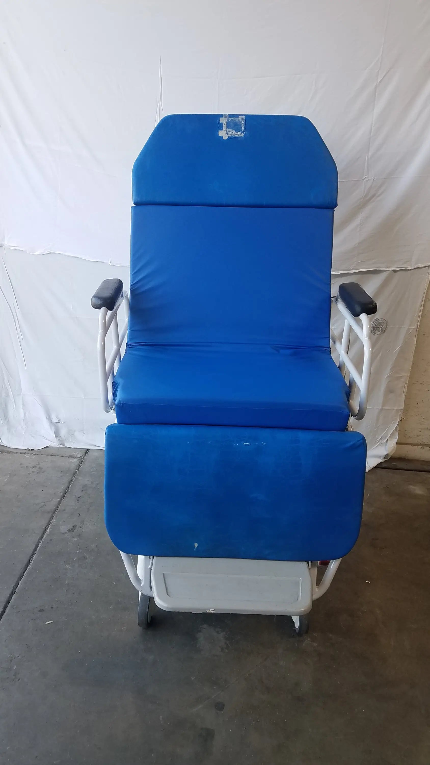 Blue padded TransMotion Medical TMM4 multi purpose stretcher chair with white metal frame and wheels for medical use
