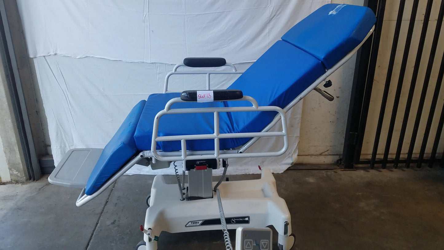 Blue padded TransMotion Medical TMM4 multi purpose stretcher chair with white metal frame and wheels for medical use