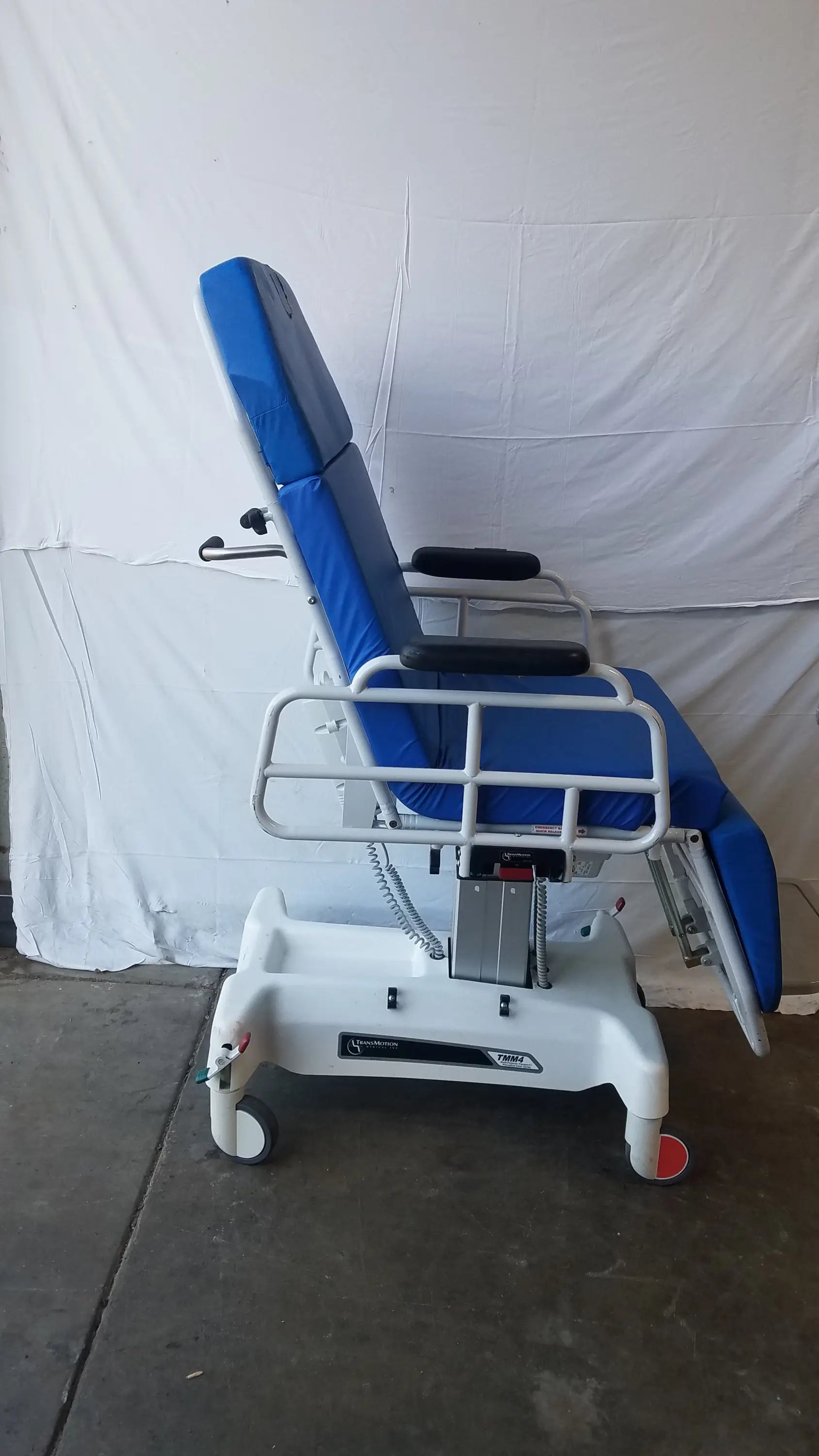 Blue padded TransMotion Medical TMM4 multi purpose stretcher chair with white metal frame and casters for medical use