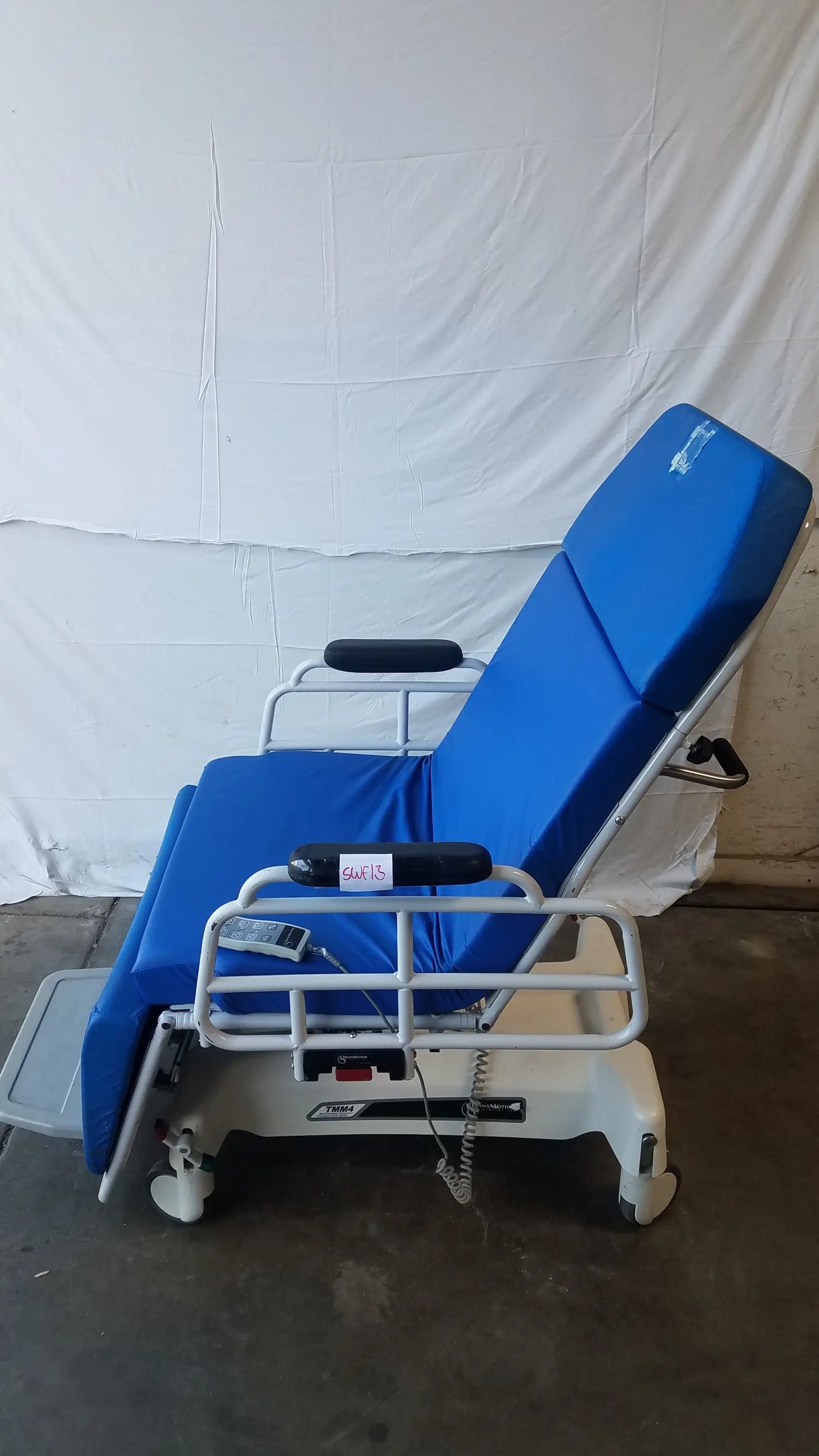 Blue padded TransMotion Medical TMM4 multi purpose stretcher chair with white metal frame and casters for medical use