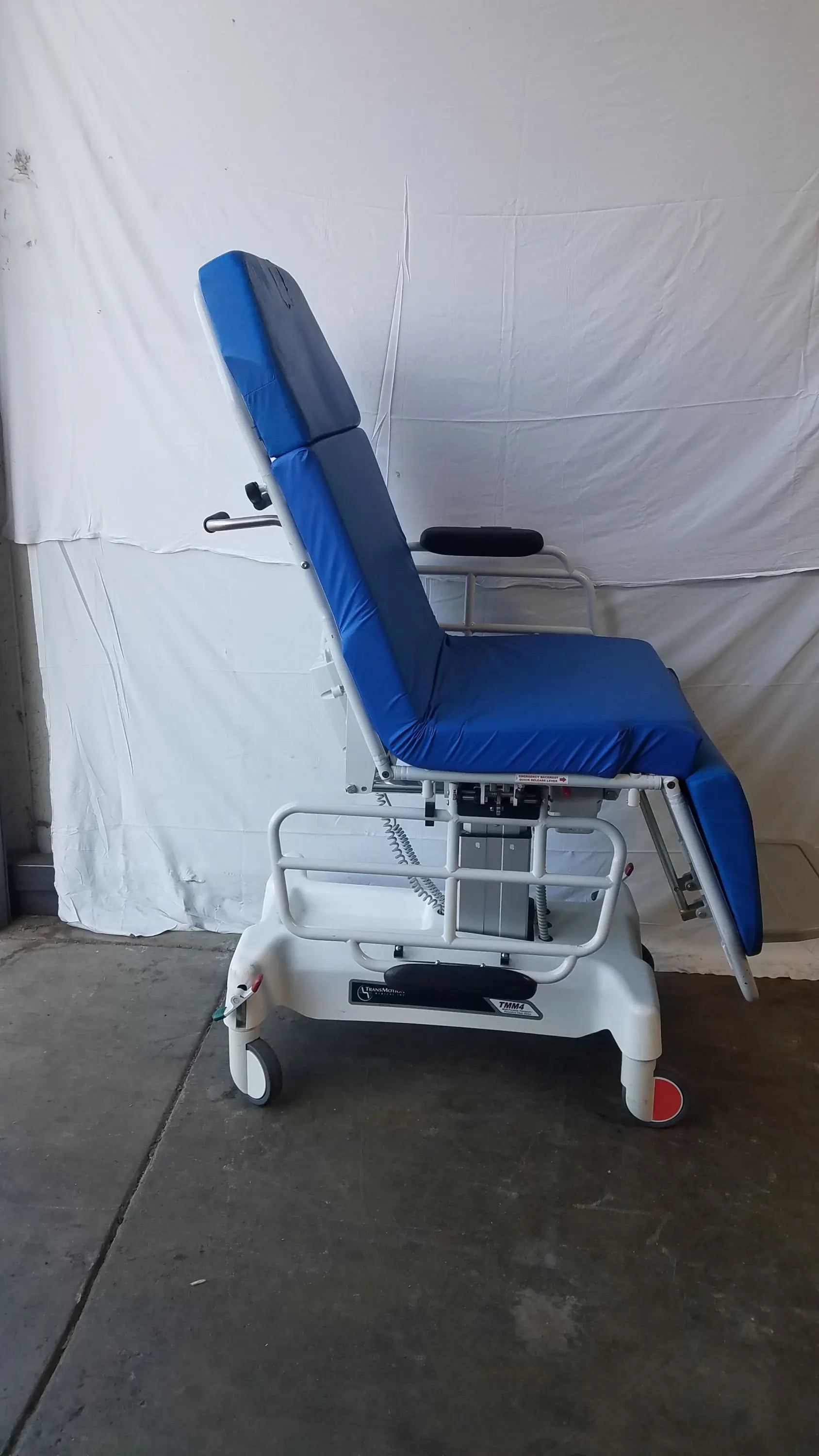 Blue padded transmotion medical tmm4 multi purpose stretcher chair with white metal frame and casters for patient care