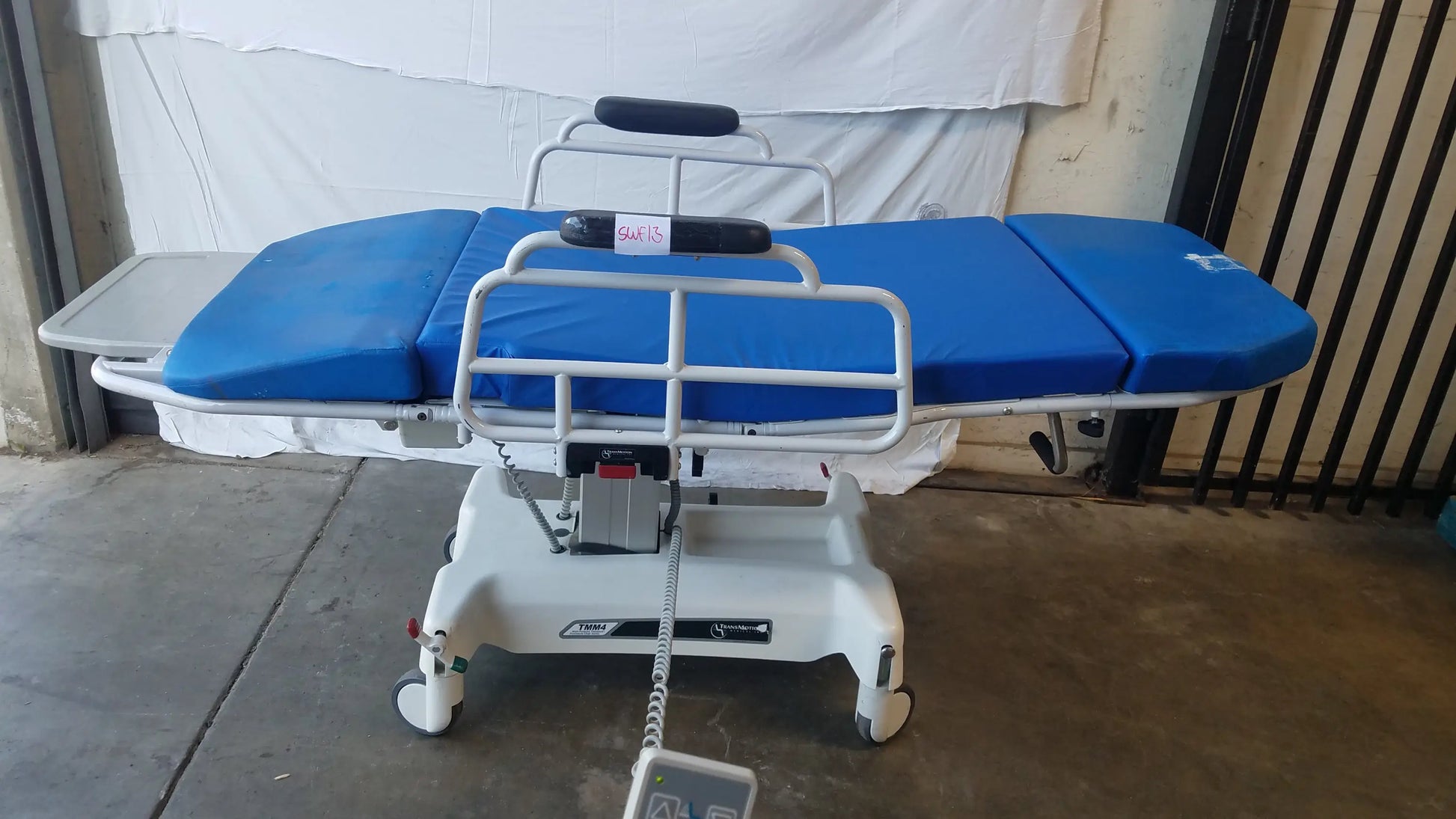 Blue padded multi purpose stretcher chair with white metal frame and wheels by TransMotion Medical TMM4