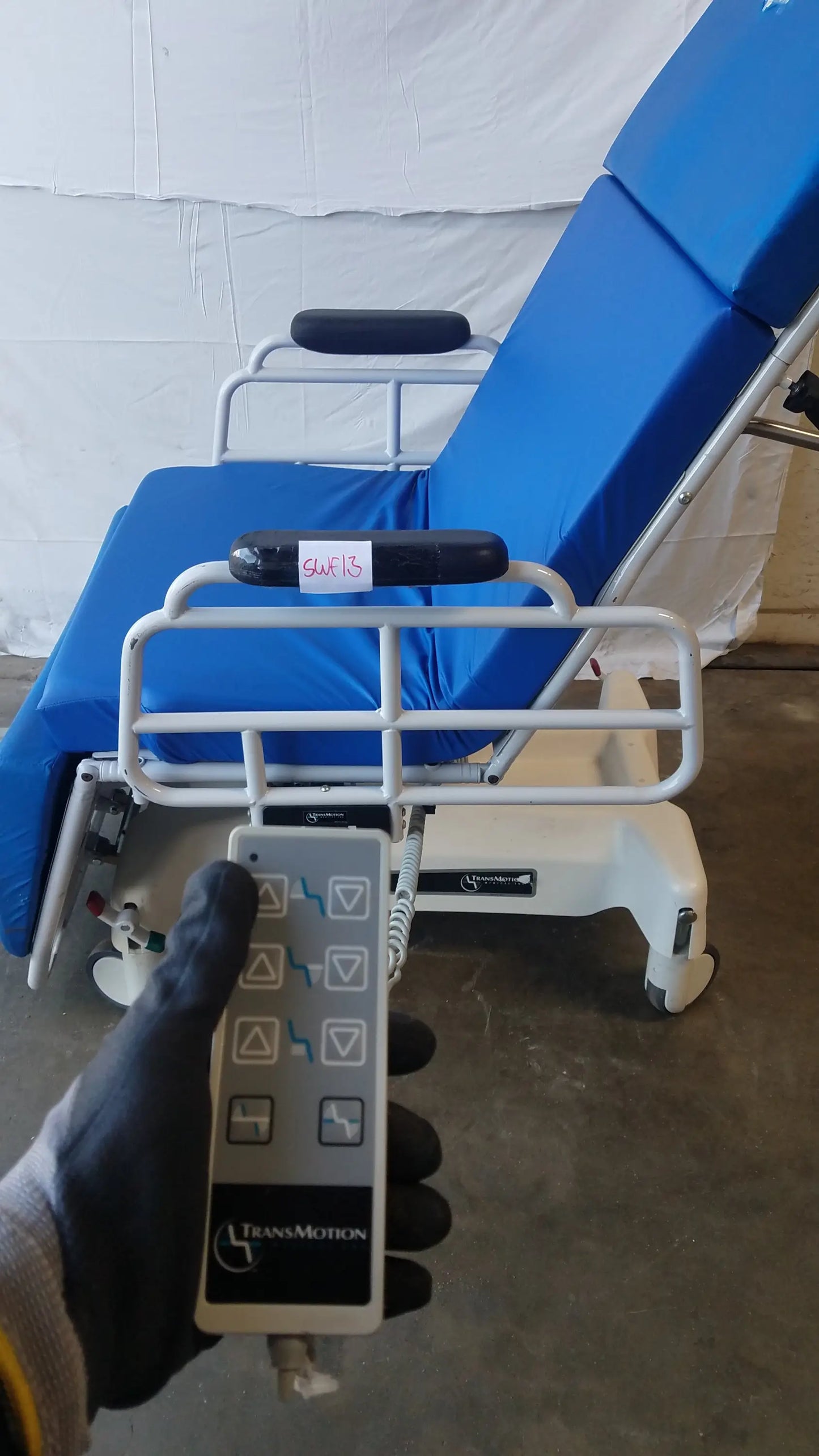 Silver remote control with black buttons branded transmotion held in gloved hand for multi purpose stretcher chair use