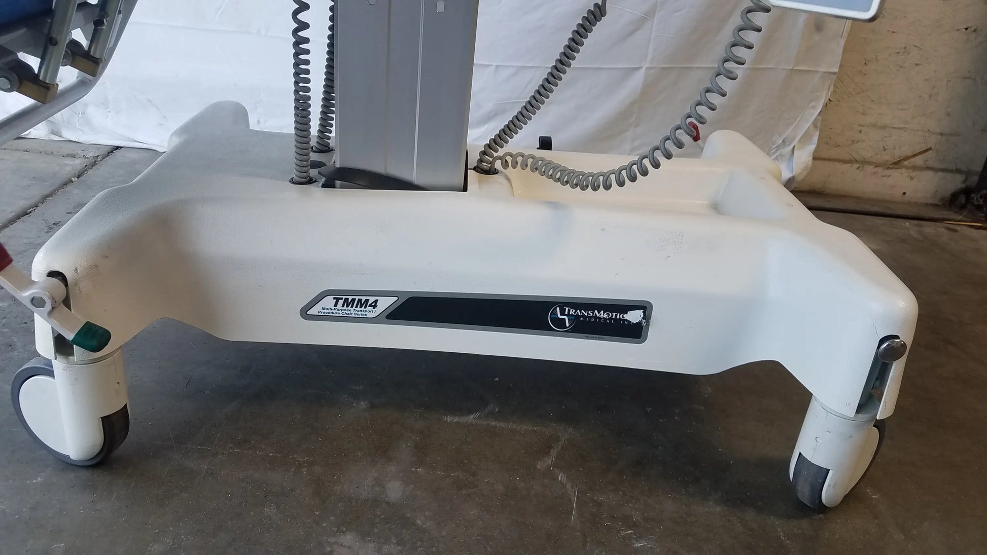 White plastic base of transmedic tmm4 multi purpose stretcher chair with four caster wheels and coiled gray cables
