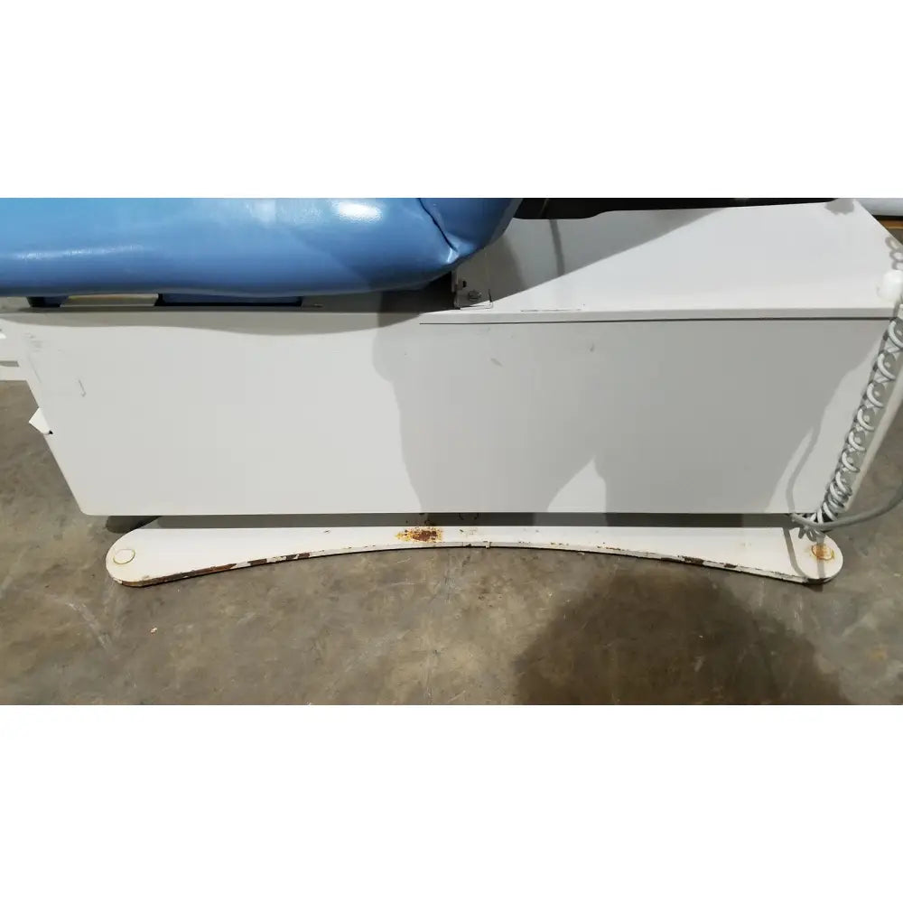 Umf 4070 power table with hand control featuring a blue upholstered top and white metal base with rusted feet medical equipment