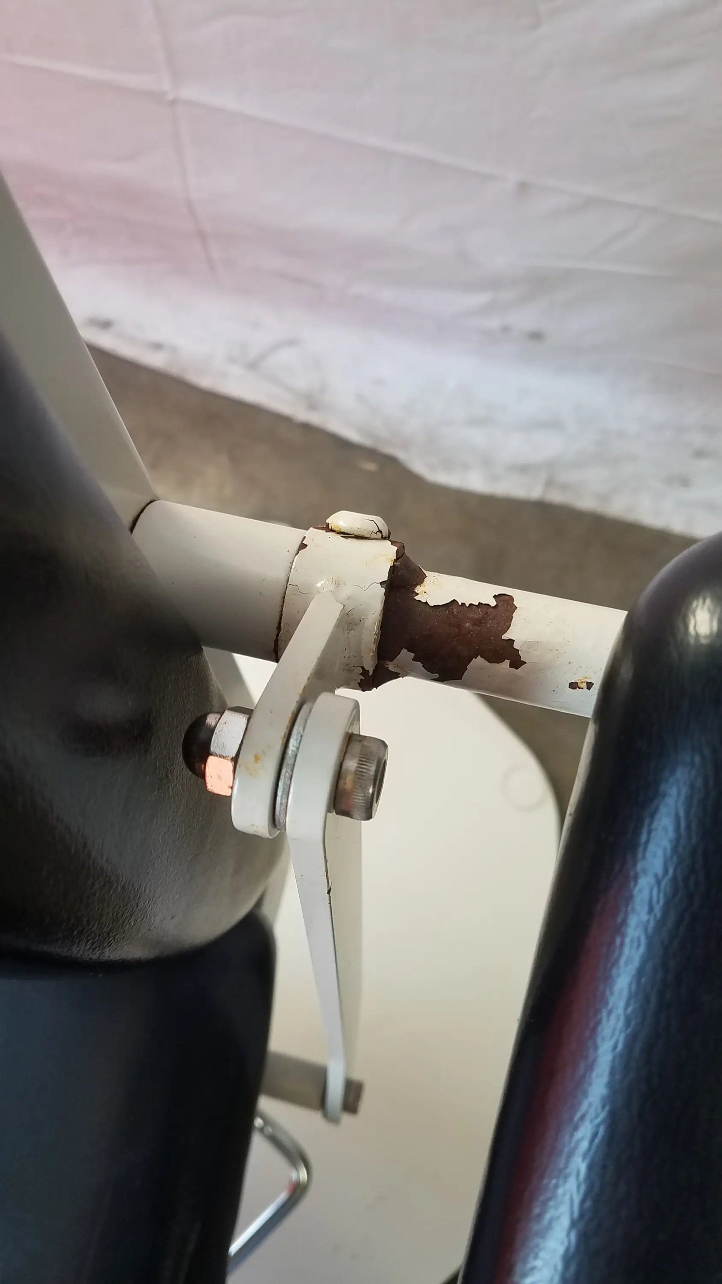 White metal bracket with rust securing cylindrical part on ums medical 8675 adjustable phlebotomy chair back side