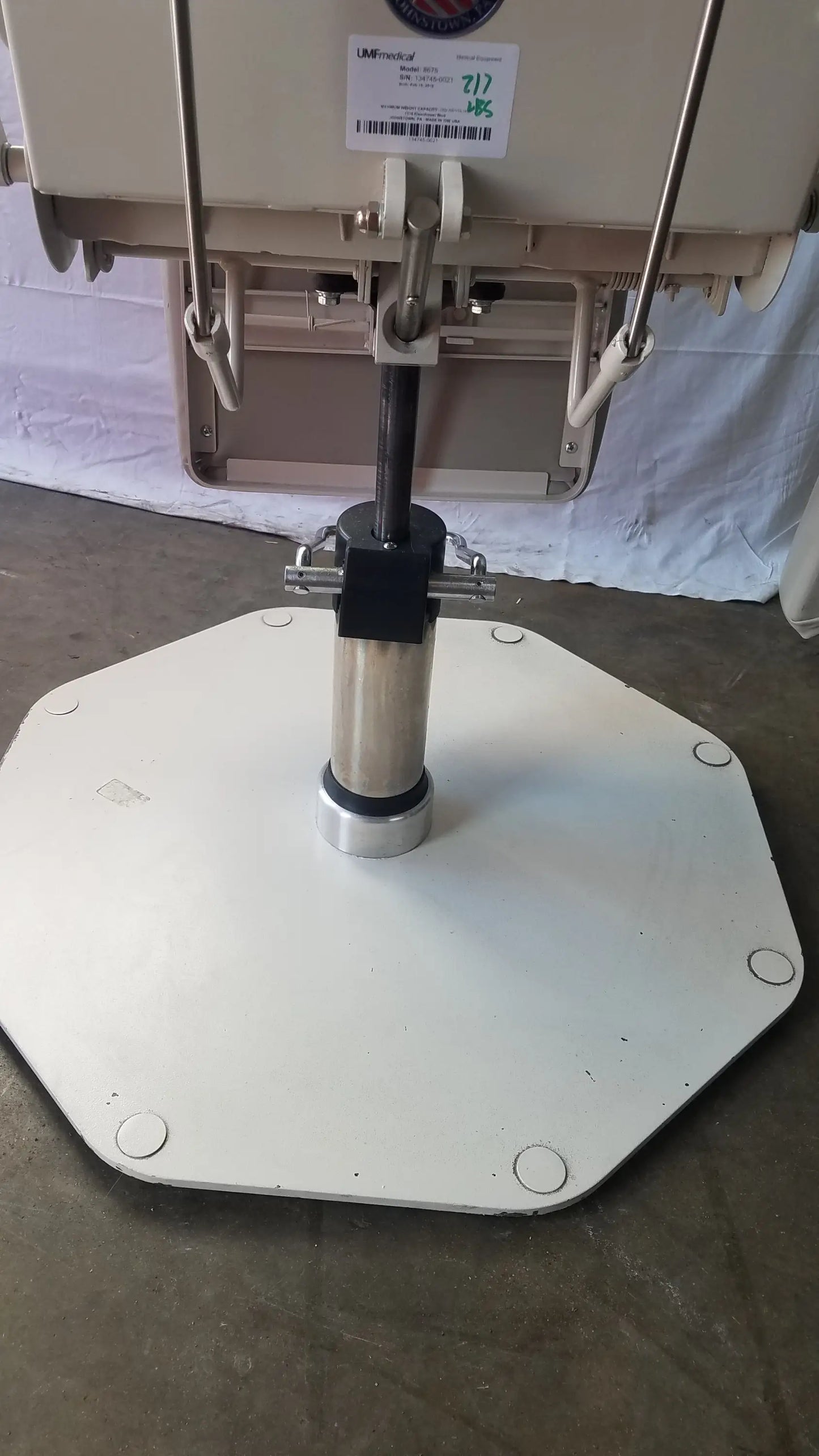 White octagonal base with central metallic cylinder and black mounting hardware of UMF Medical adjustable phlebotomy chair